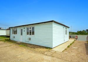 a small white building with a roof on a road at Sailing Club Bungalow in Wolferton