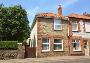 a brick house with white windows on a street at Silvergate Cottage in West Runton