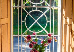 un jarrón de flores sentado frente a una ventana en South Lodge East, en Holkham