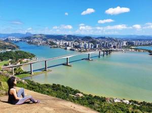 a man sitting on a rock looking at a bridge over a river at SUÍTE Princípio in Vila Velha