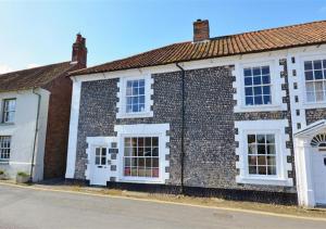 a brick building with white doors and windows on a street at The Old Bakery in Blakeney