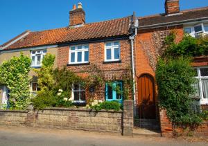 a red brick house with a gate and bushes at Wren Cottage in Aylsham