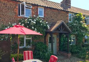 a red umbrella and chairs in front of a brick house at Thimble Cottage in Dersingham