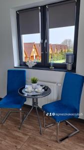 a dining room with blue chairs and a table and two windows at Sunset Beach in Sarbinowo