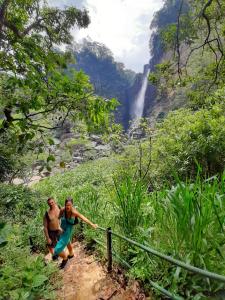 duas pessoas a andar por um trilho em frente a uma cascata em Pine Trees Homestay em Nallathanniya