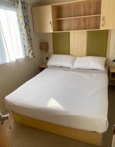 um quarto com uma cama grande com lençóis brancos e uma janela em Beach Caravan Holiday Home em Mablethorpe