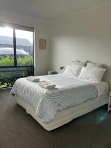 a white bedroom with a large bed with a window at Purangi Beachhouse in Cooks Beach