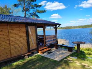 eine Hütte mit einer Terrasse neben einem See in der Unterkunft Siedlisko nr 2 nad jeziorem Skarlińskim, jezioro, mazury, domki letniskowe in Kurzętnik