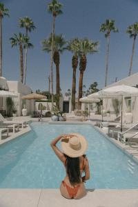 Yara Hotel - Adults Only في بالم سبرينغز: امرأة ترتدي قبعة تجلس أمام حمام السباحة