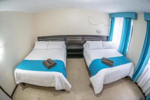 two beds in a small room with blue curtains at Hotel Tungurahua in Baños