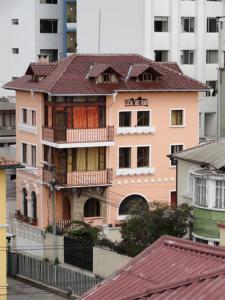 a pink building with a red roof in a city at Hostal San Juan in Quito