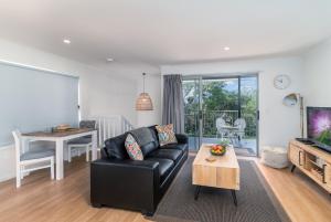 a living room with a black leather couch and a table at Little Bank House in Mount Tamborine