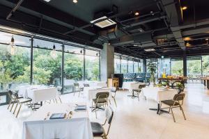 een restaurant met witte tafels, stoelen en ramen bij Hotel BEGINS 倉箱蜜境文旅 in Keelung