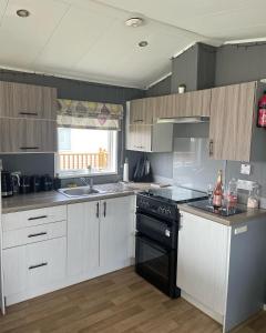 a kitchen with white cabinets and a black stove top oven at Lake District Modern Static Caravan in Maryport