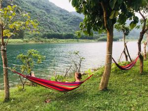 a man laying in a hammock next to a lake at Phong Nha A Little Leaf Homestay in Phong Nha
