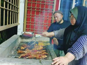 un hombre y una mujer cocinando comida en una parrilla en CHALET MERAH MERIAM, YAN KEDAH, en Yan