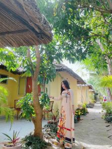 a woman in a dress standing next to a tree at Thuy - Gunter Garden Bungalow in Mui Ne