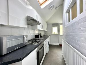 una cucina con armadi bianchi e piano cottura di Massive 4 bedroom Duplex Apartment - Sleeps up to 10 People - Free Parking - 5 Minutes to the Best Beach! - Great Location - Fast WiFi - Smart TV - Newly decorated - sleeps up to 10! Close to Bournemouth & Poole Town Centre & Sandbanks a Bournemouth