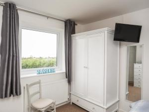 a bedroom with a window and a chair and a cabinet at 2 Y Bont in Pentraeth