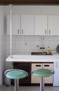 a kitchen with white cabinets and two green bar stools at Mileva apartman in Kikinda