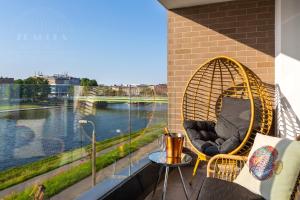 a wicker chair sitting on a balcony overlooking a river at Fragola Apartments Vistula View in Kraków