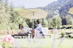 two women sitting on chairs under an umbrella at Hotel Habicher Hof 4-Sterne-Superior in Oetz