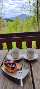 a wooden table with two cups and a slice of cake at Caputówka 100 letnia chata in Rajcza