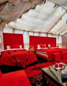 a red bedroom with two beds and a table at Merzouga Sahara Camp in Merzouga