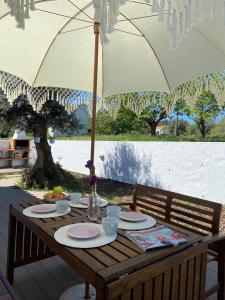 a wooden table with plates and an umbrella at QUINTA DAS TEIMOSAS by Stay in Alentejo in Cercal