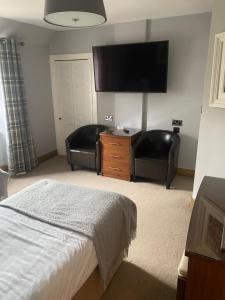 a bedroom with a bed and two chairs and a flat screen tv at Garden Rooms in Pitlochry