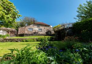 an old stone house with a bridge in a garden at Court Cottage in Berrynarbor