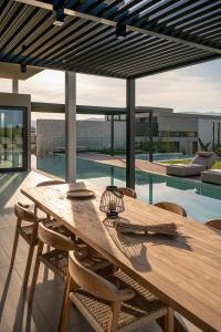 mesa de comedor de madera con sillas y piscina en Pnoe Villas - Seafront Experience en Tavronitis