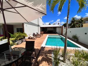 a swimming pool with chairs and an umbrella next to a house at VilaMar Jacuípe in Camaçari