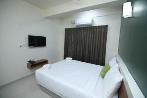 a small bedroom with a white bed and a television at Hotel Royal Blooms in Bangalore