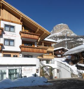 a snow covered building with a mountain in the background at Pension Garden Hotel in Colfosco