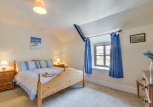 a bedroom with a bed and a window with blue curtains at Waterside Cottage Westleigh in Westleigh