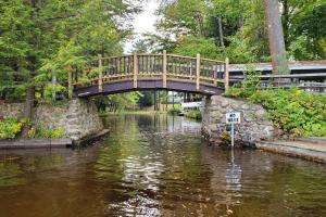 un puente de madera sobre un río con un río en The Stabbin Cabin on Grant Island Brantingham Lake, en Glenfield