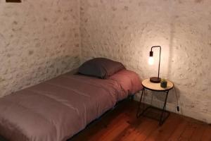 a small room with a bed and a table with a lamp at Maison charentaise à la campagne in Bécheresse