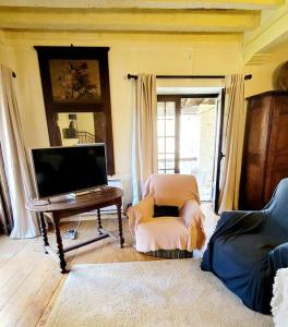 ein Wohnzimmer mit einem TV, einem Stuhl und einem Klavier in der Unterkunft Le Moulin de la Rode in Coly