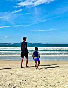 Un hombre y un niño caminando por la playa en FLAT / APARTAMENTO NA PRAIA DO FORTE en Cabo Frío