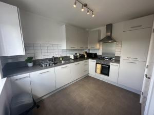 a kitchen with white cabinets and a sink and a stove at 3 Bed Home for Contractors & Relocators with Parking, Garden & WiFi 5 mins walk to Town Centre & Train Station in Stafford