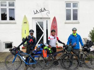 três homens de pé ao lado de suas bicicletas em frente a um edifício em La Ola em Hanstholm