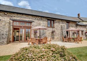 ein Steinhaus mit einem Tisch, Stühlen und Sonnenschirmen in der Unterkunft Threshing Barn in Bampton