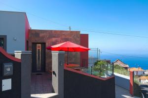 ポンタ・ド・ソルにある2 bedrooms house with sea view furnished terrace and wifi at Ponta do Sol 5 km away from the beachの家のバルコニーに座る赤い傘
