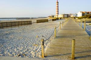 een houten promenade die leidt naar een vuurtoren op een strand bij One bedroom apartement with city view balcony and wifi at Gafanha da Nazare in Gafanha da Nazaré