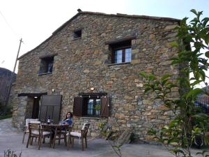 una mujer sentada en una mesa frente a un edificio de piedra en 2 bedrooms house with furnished garden at Las Colladas, en Las Colladas