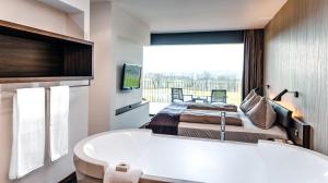 a bathroom with a tub and a bed and a television at Wellnesshotel Golf Panorama in Lipperswil