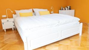 ein weißes Bett in einem Schlafzimmer mit orangefarbener Wand in der Unterkunft B&B Gösselsdorfer Seeblick in Sittersdorf