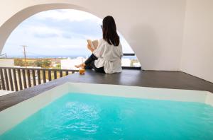 une femme assise sur un balcon pour lire un livre à côté d'une piscine dans l'établissement WHITE BREEZE VILLAS, à Éxo Goniá