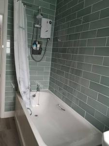 een groene betegelde badkamer met een bad en een douche bij The Old Police Station in Hatherleigh